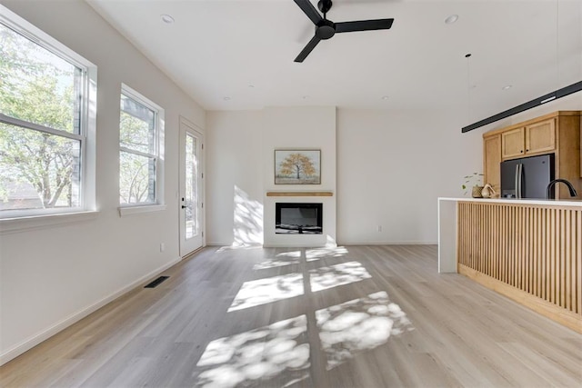 577 S Fretz Ave, Edmond, OK 73003 - unfurnished living room featuring light wood-type flooring, a ceiling fan, a sink, a glass covered fireplace, and baseboards