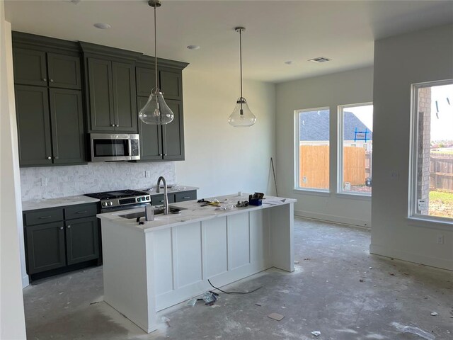 kitchen with appliances with stainless steel finishes, decorative backsplash, concrete floors, hanging light fixtures, and a kitchen island with sink