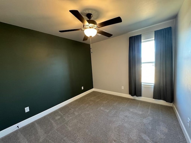 spare room featuring ceiling fan, dark colored carpet, and baseboards