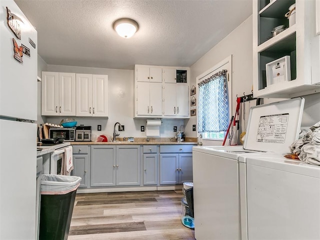 washroom featuring washing machine and clothes dryer, light wood-style floors, a textured ceiling, and cabinet space