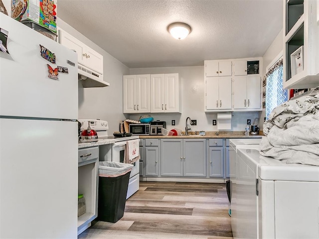 kitchen with white appliances, white cabinetry, light wood-style flooring, a textured ceiling, and under cabinet range hood