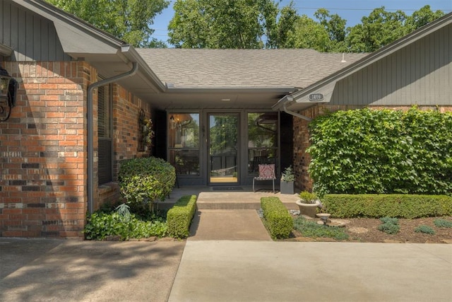 view of exterior entry with brick siding and a shingled roof