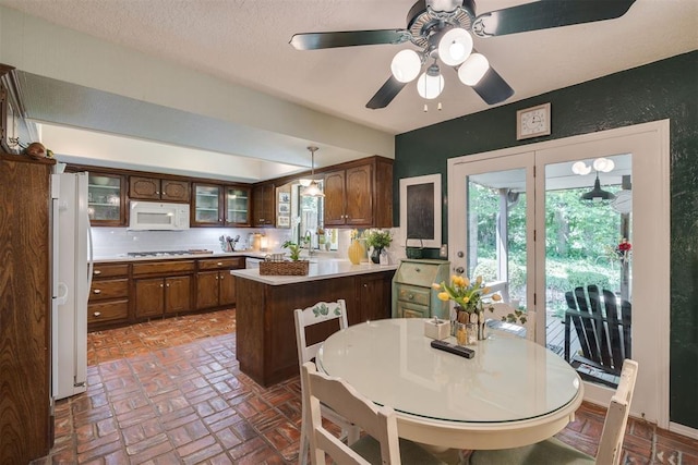 kitchen with white appliances, a peninsula, brick floors, light countertops, and glass insert cabinets