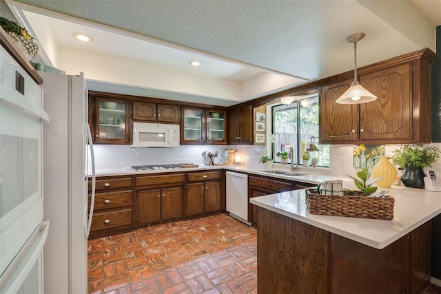 kitchen featuring white appliances, a sink, a peninsula, brick floors, and backsplash