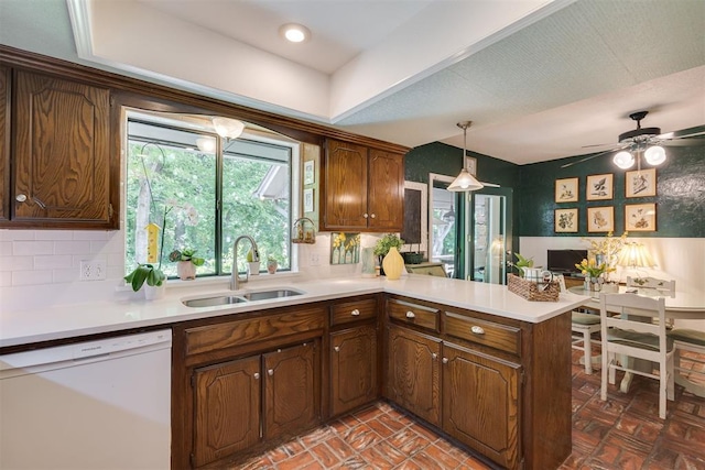 kitchen featuring white dishwasher, a sink, a peninsula, and light countertops