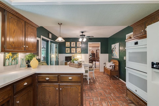 kitchen with a peninsula, double oven, light countertops, a ceiling fan, and decorative light fixtures