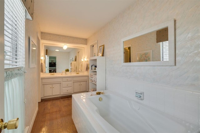 full bath with wood finished floors, a bath, wallpapered walls, and double vanity