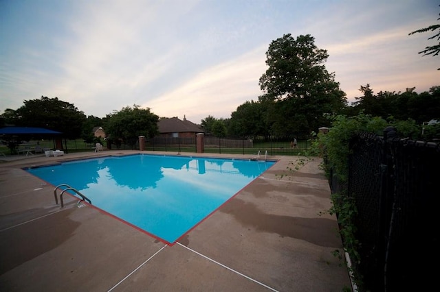 pool at dusk featuring a patio, fence, and a community pool