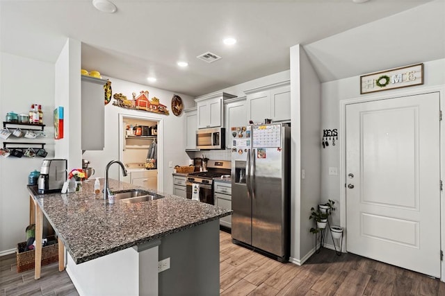 12509 NE 36th Sts, Spencer, OK 73084 - kitchen featuring stainless steel appliances, a sink, a peninsula, dark stone counters, and wood finished floors