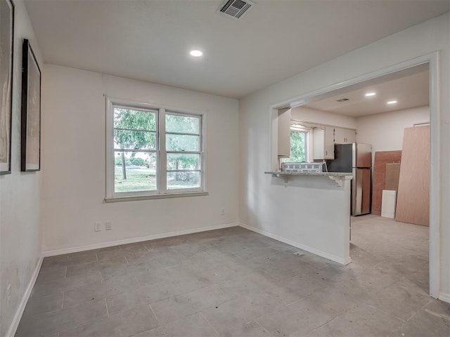 kitchen with healthy amount of natural light, freestanding refrigerator, a breakfast bar, a peninsula, and recessed lighting