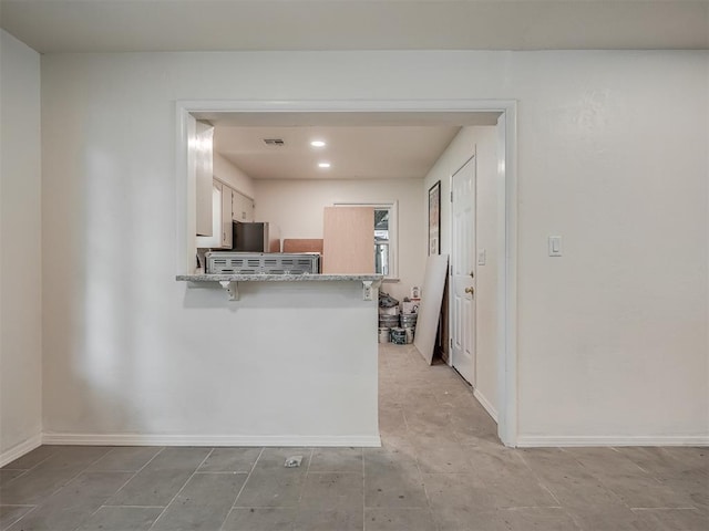 kitchen with a peninsula, fridge, light stone countertops, baseboards, and white cabinetry