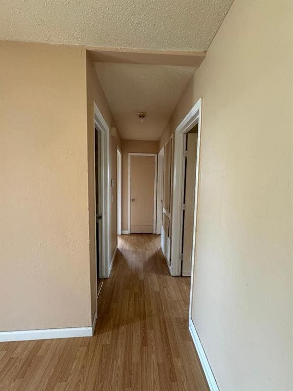 hallway with wood finished floors, baseboards, and a textured ceiling