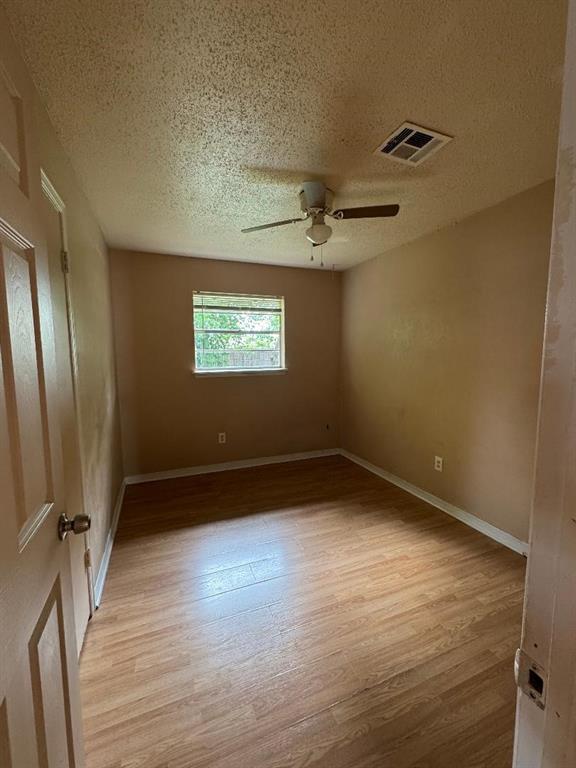 spare room with light wood-type flooring, ceiling fan, a textured ceiling, and baseboards
