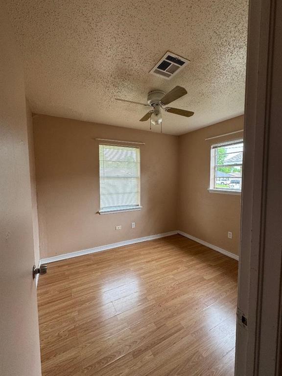empty room featuring a textured ceiling, light wood finished floors, a ceiling fan, and baseboards