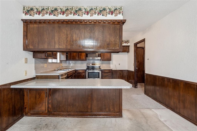 3109 N Glade Ave, Bethany, OK 73008 - kitchen featuring appliances with stainless steel finishes, a peninsula, light countertops, wood walls, and wainscoting