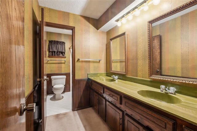3109 N Glade Ave, Bethany, OK 73008 - full bath with wallpapered walls, toilet, double vanity, a wainscoted wall, and tile patterned floors