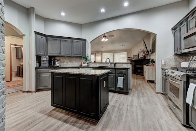 17009 Picasso Dr, Oklahoma City, OK 73170 - kitchen with appliances with stainless steel finishes, arched walkways, a center island, a ceiling fan, and light wood finished floors