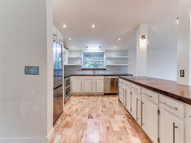kitchen with appliances with stainless steel finishes, open shelves, a sink, white cabinets, and tasteful backsplash