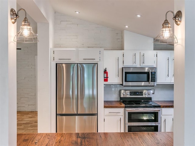 kitchen featuring stainless steel appliances, lofted ceiling, tasteful backsplash, white cabinetry, and wood finished floors
