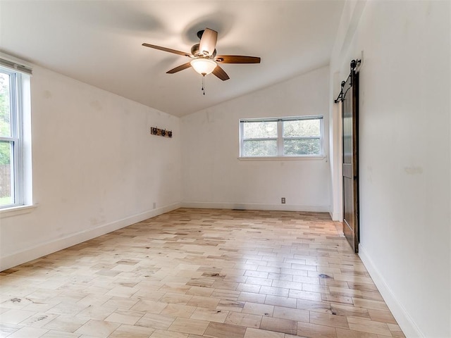 spare room featuring a ceiling fan, lofted ceiling, a barn door, and baseboards
