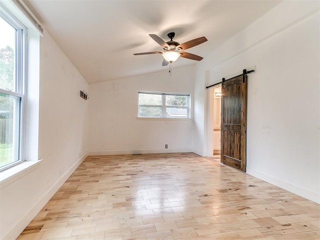 empty room with ceiling fan, vaulted ceiling, a barn door, light wood finished floors, and baseboards