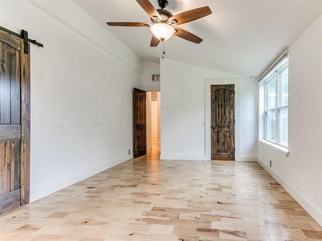 spare room featuring lofted ceiling, a barn door, a ceiling fan, baseboards, and light wood-type flooring