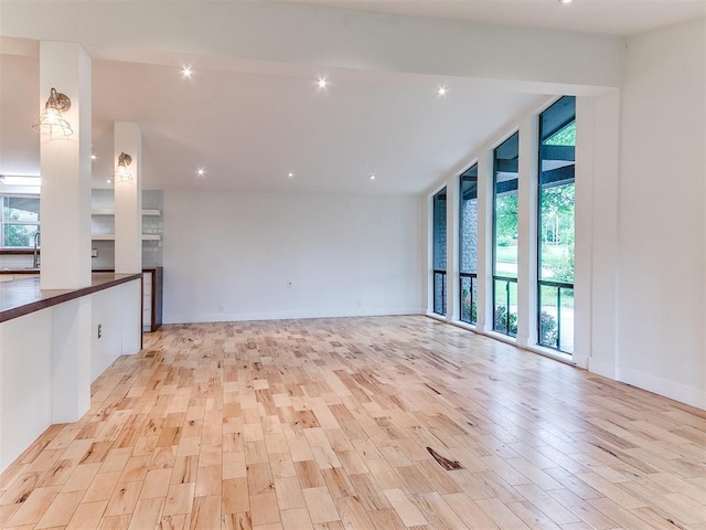 empty room with light wood-style flooring, a wall of windows, a sink, recessed lighting, and baseboards