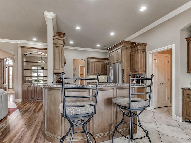 12515 Forest Oaks Dr, Choctaw, OK 73020 - kitchen with arched walkways, stainless steel refrigerator with ice dispenser, a kitchen breakfast bar, ornamental molding, and light stone counters