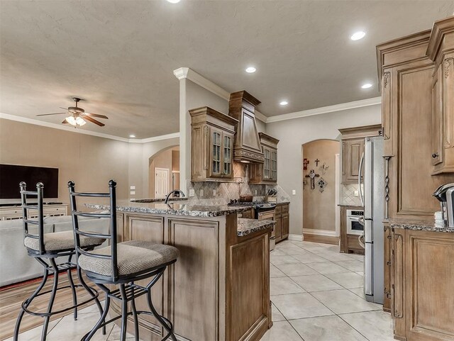 12515 Forest Oaks Dr, Choctaw, OK 73020 - kitchen with premium range hood, arched walkways, appliances with stainless steel finishes, a kitchen bar, and a peninsula