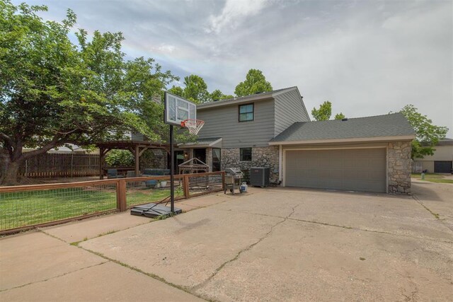 11412 Leaning Elm Rd, Oklahoma City, OK 73120 - view of front of property with stone siding, concrete driveway, fence, an attached garage, and cooling unit