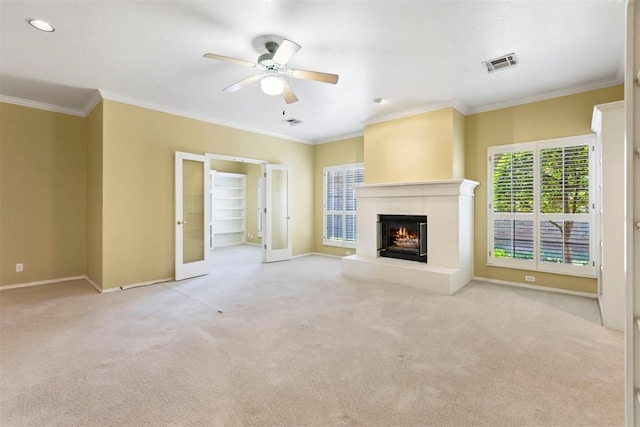 unfurnished living room with ceiling fan, carpet flooring, baseboards, a warm lit fireplace, and ornamental molding