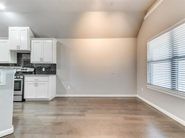 2408 Santa Monica St, Edmond, OK 73034 - kitchen with stainless steel gas stove, vaulted ceiling, decorative backsplash, white cabinets, and light wood-style flooring