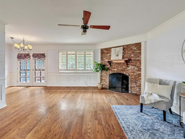 6120 Kingston Rd, Oklahoma City, OK 73122 - living room featuring wood finished floors, a chandelier, a ceiling fan, a brick fireplace, and ornamental molding