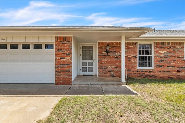 doorway to property featuring brick siding, a garage, concrete driveway, a yard, and roof with shingles