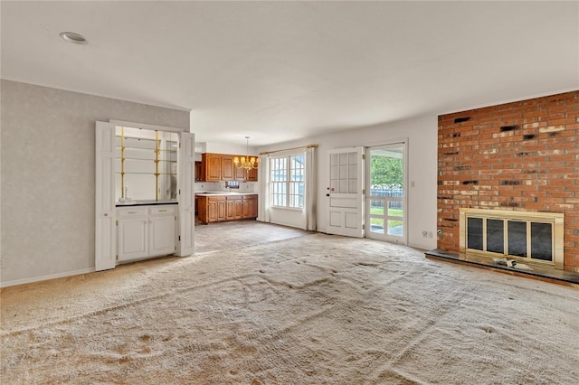 unfurnished living room with a chandelier, a brick fireplace, light carpet, and baseboards