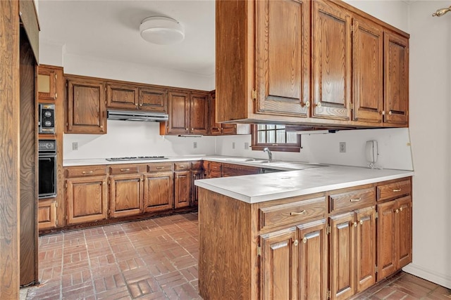 kitchen featuring brown cabinetry, oven, under cabinet range hood, and a peninsula
