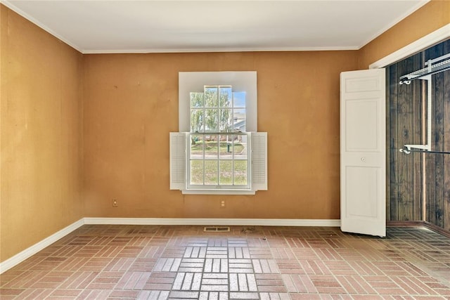 spare room featuring brick flooring, baseboards, and ornamental molding