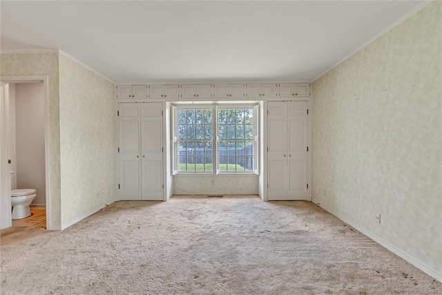 unfurnished bedroom with carpet, wallpapered walls, ornamental molding, baseboards, and connected bathroom