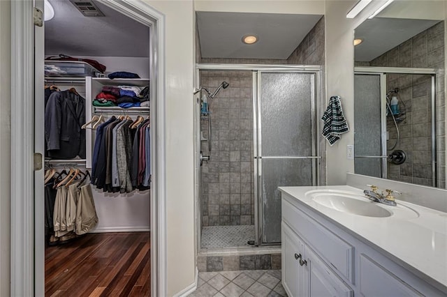 3001 NE 129th St, Edmond, OK 73013 - bathroom with vanity, a shower stall, a walk in closet, wood finished floors, and baseboards