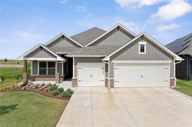 craftsman house with a shingled roof, an attached garage, driveway, and a front yard