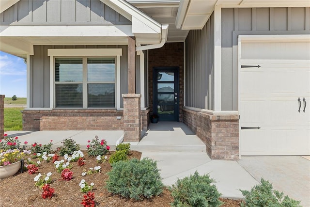 doorway to property with board and batten siding, brick siding, an attached garage, and a porch