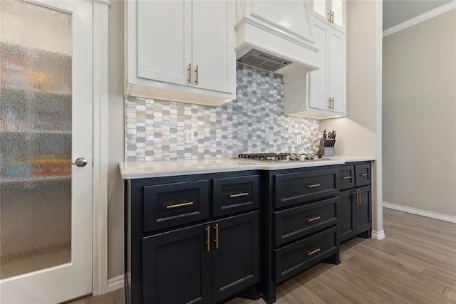 kitchen with premium range hood, white cabinets, stainless steel gas stovetop, light countertops, and ornamental molding