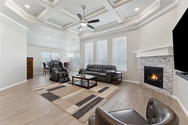living area with a ceiling fan, wood finished floors, a stone fireplace, ornamental molding, and beamed ceiling