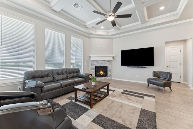 living room with a ceiling fan, coffered ceiling, light wood-style floors, crown molding, and a stone fireplace