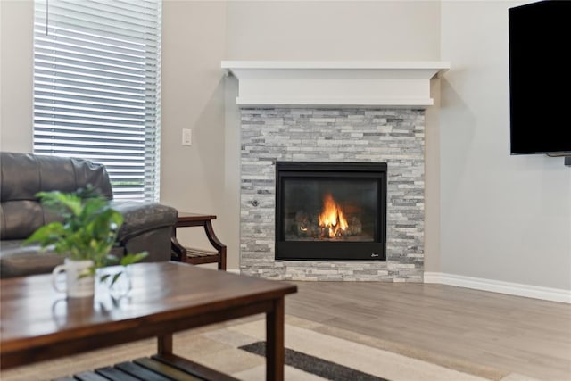 living area with a stone fireplace, wood finished floors, and baseboards