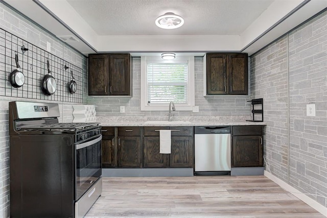1316 W Logan Ave, Guthrie, OK 73044 - kitchen featuring stainless steel appliances, a sink, dark brown cabinets, a textured ceiling, and brick wall