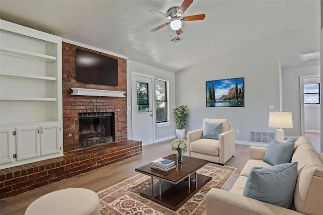 living area with wood finished floors, a ceiling fan, a brick fireplace, baseboards, and vaulted ceiling