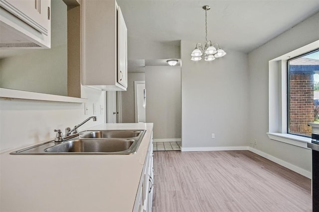 kitchen featuring a sink, white cabinets, a chandelier, light wood-type flooring, and hanging light fixtures