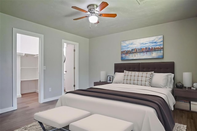 bedroom with wood finished floors, a walk in closet, baseboards, a ceiling fan, and a closet
