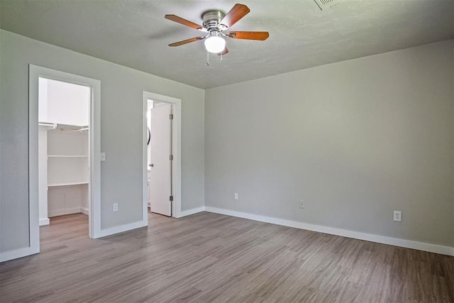 unfurnished bedroom featuring a spacious closet, wood finished floors, baseboards, a closet, and ceiling fan